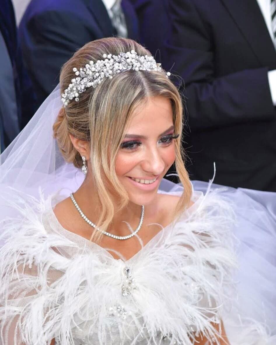 A smiling bride in a crystal tiara and a feathered gown, her skin softly bronzed